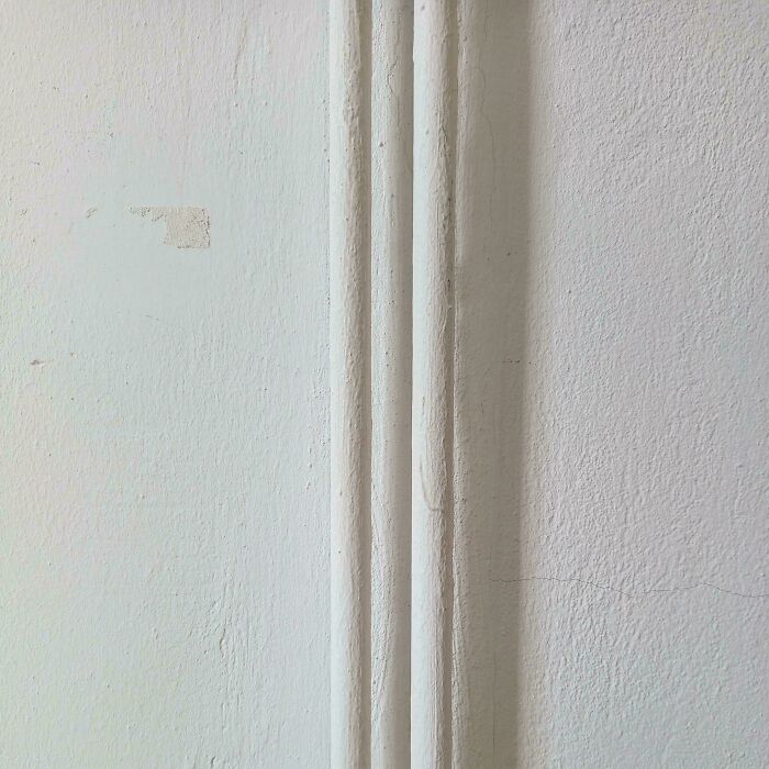Confusing perspective of a white wall with vertical pipes that blend in, creating an optical illusion.