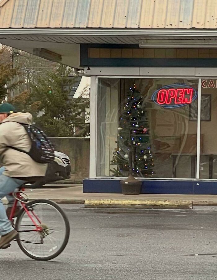Confusing perspective with a cyclist appearing to ride through a Christmas tree inside a store with an 
